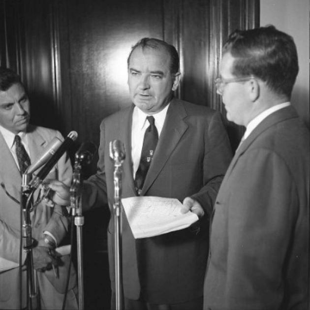 McCarthy talking at a microphone 