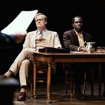 White man and black man sitting at a table looking very solemn