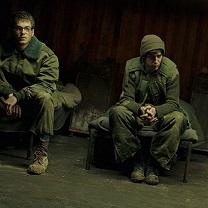 Two young white men in military uniforms sitting dejectedly on a bench