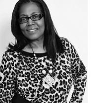 Black and white photo of a black woman with shoulder length hair, black rimmed glasses, a leopard print top and a necklace