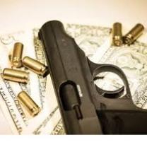 Dark gray handgun lying sideways on a table with gold bullets strewn around it