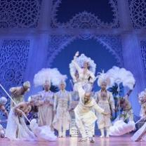 Fancy costumed people against blue theater backdrop like a castle inside, feathered headdresses, dancing