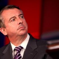 Middle aged white guy with receding brown hair looking sideways with a worried look on his face, wearing a gray suit with a purple and white striped tie