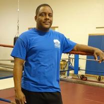 Black man in blue t-shirt standing next to a boxing ring