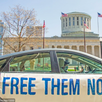 Car with sign saying Free Them Now in front of Ohio Statehouse