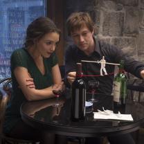 Man and woman sitting at a table looking at small replica of man on a wire between two towers