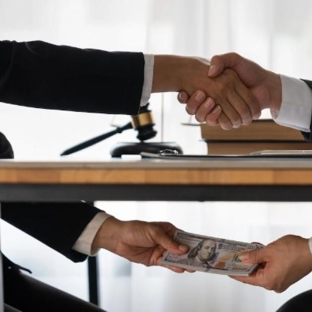 Two men shaking hands above the table and exchanging money under the table