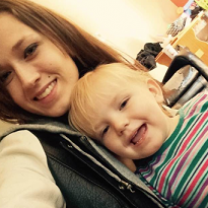 Young white woman with straight brown hair smiling and holding a blonde girl baby