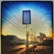 Blue background sky with a tall rectangular sign that is blank on a city street