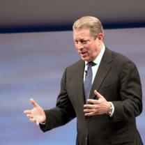 White man with graying dark hair in a suit holding his arms out in emphasis as he talks