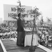 Guy at a platform speaking to a crowd with sign No More Hiroshimas