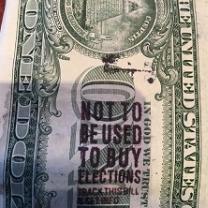 A close up of the back of a dollar bill with a stamp on it saying Not to be used to buy elections